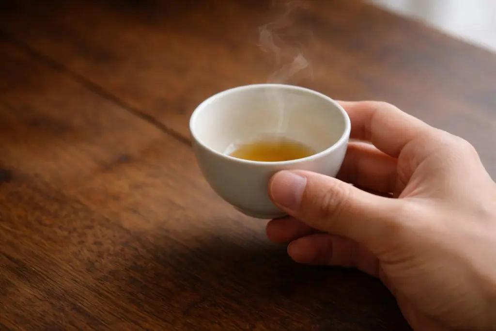 Bàn tay cầm chén trà nhỏ trên nền bàn gỗ