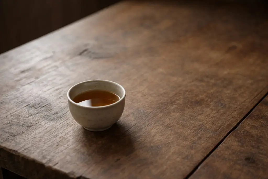 Chén trà nước màu vàng nâu đặt trên bàn gỗ cũ trong ánh sáng nghiêng tự nhiên