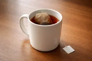 Cốc sứ trắng với túi lọc trà đang ngâm trên bàn gỗ trong ánh sáng tự nhiên